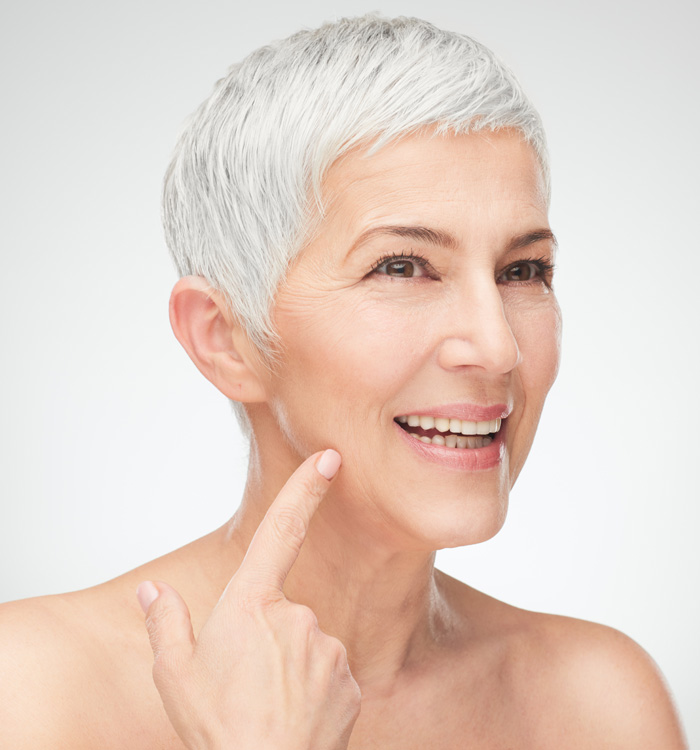 A smiling older woman touching side of her cheek